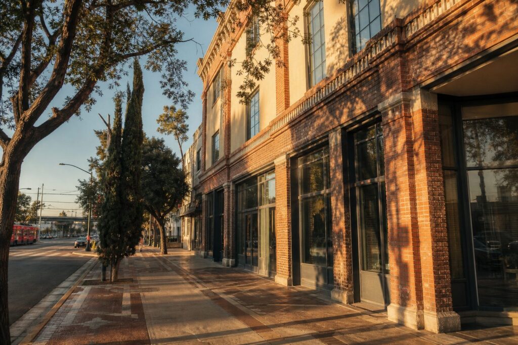 Mixed-use brick loft building in Little Italy San Diego with historic storefronts and mature street trees along sidewalk.